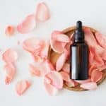 Top view of empty brown bottle for skin care product placed on wooden plate with fresh pink rose petals on white background isolated