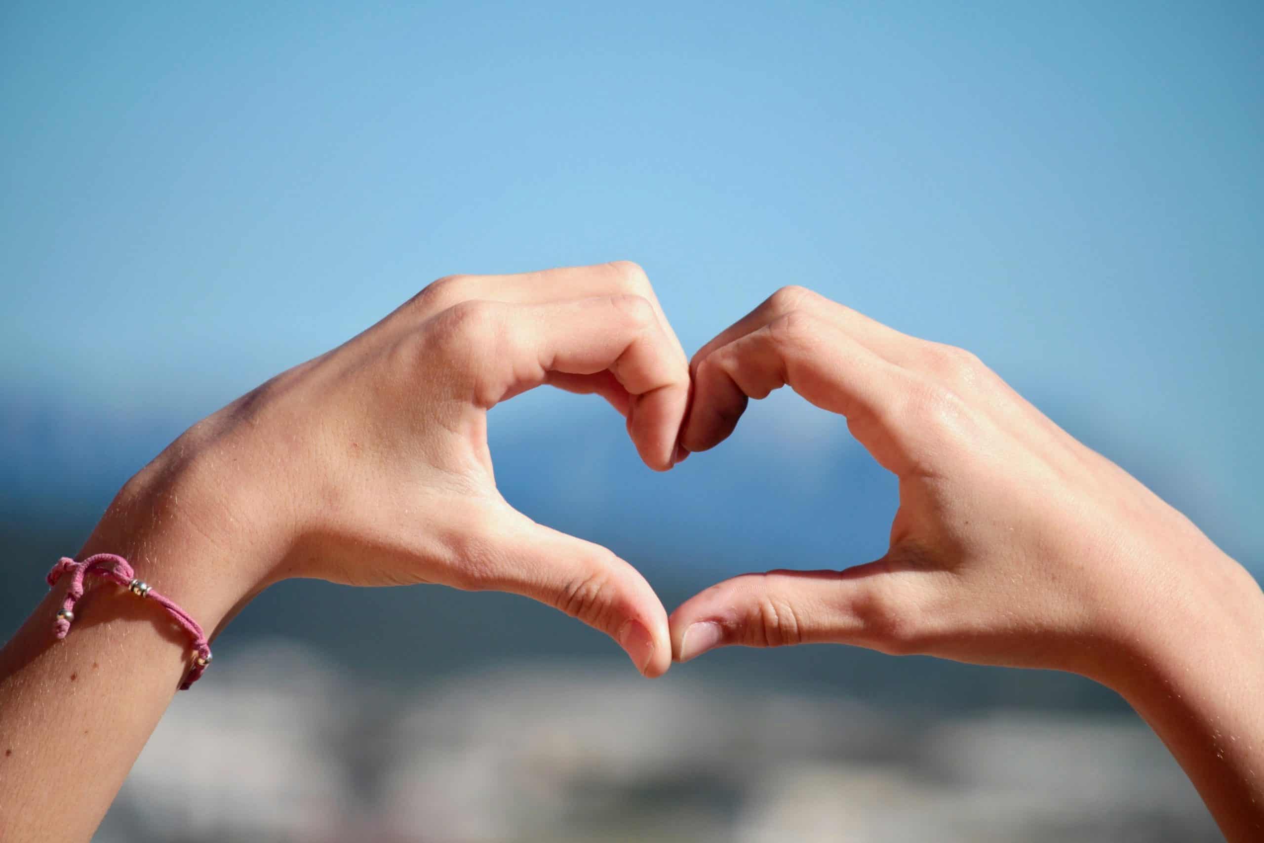 Close-up of hands forming a heart shape with clear blue sky background.
