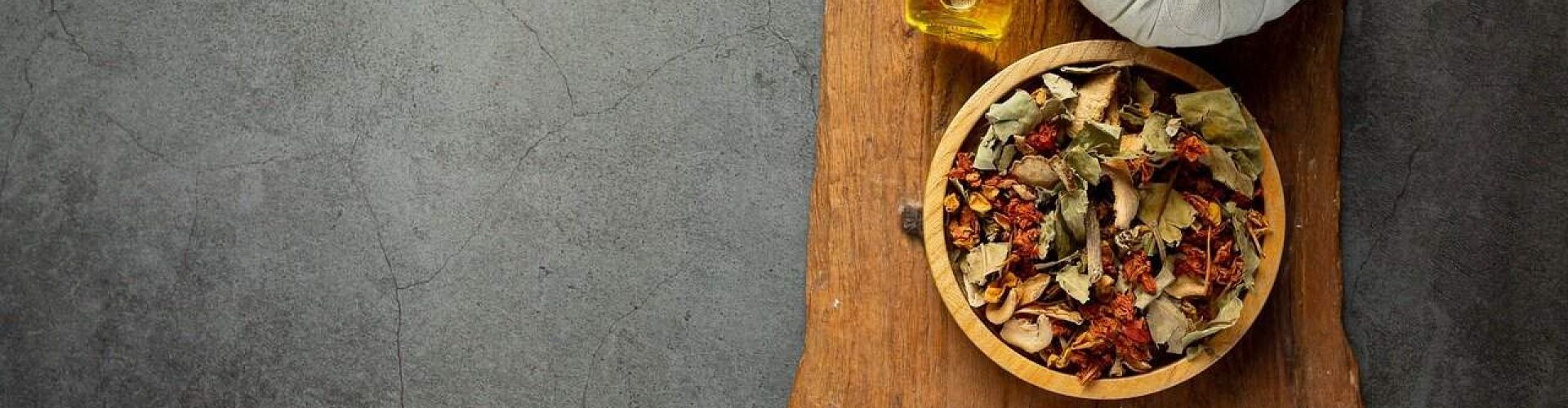 Holistic therapy essentials including herbs, oil, and towel on wooden board.